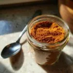 A glass jar filled with homemade taco seasoning, with a spoon to the left.