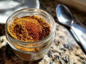 A close-up of homemade taco seasoning in a glass jar, with a spoon blurred in the background.