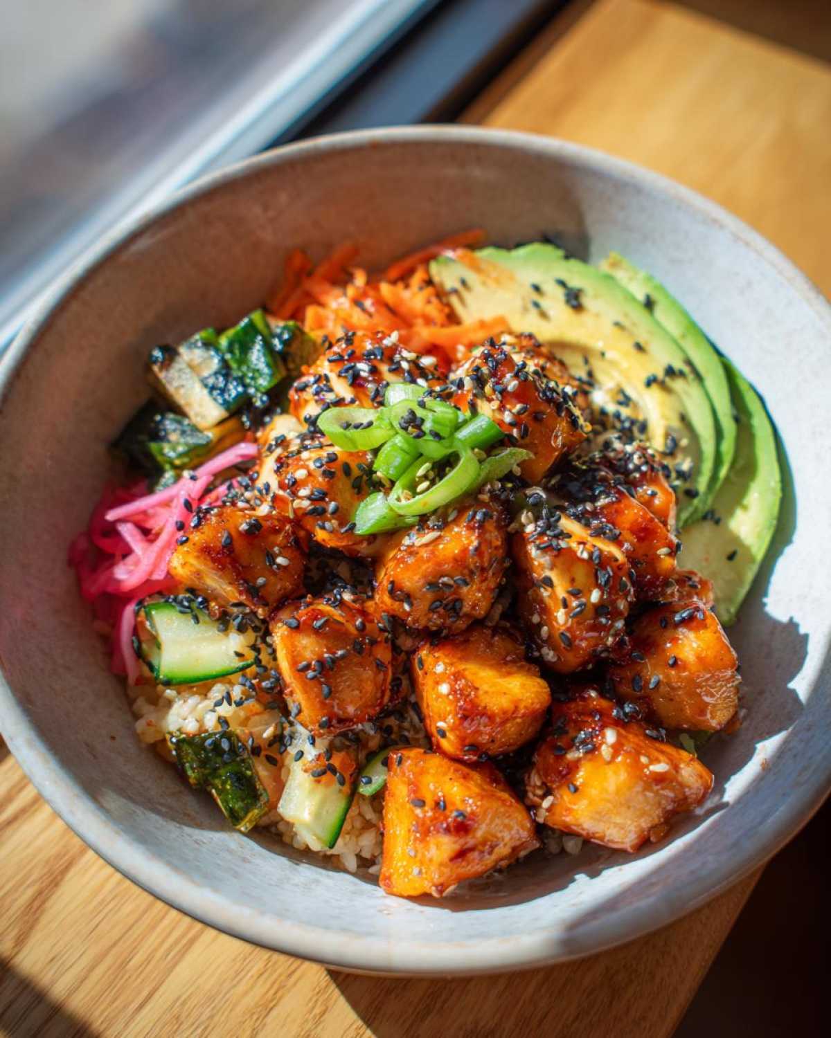 A vibrant Hot Honey Chicken Bowl featuring glazed chicken, sliced avocado, shredded carrots, and zucchini.