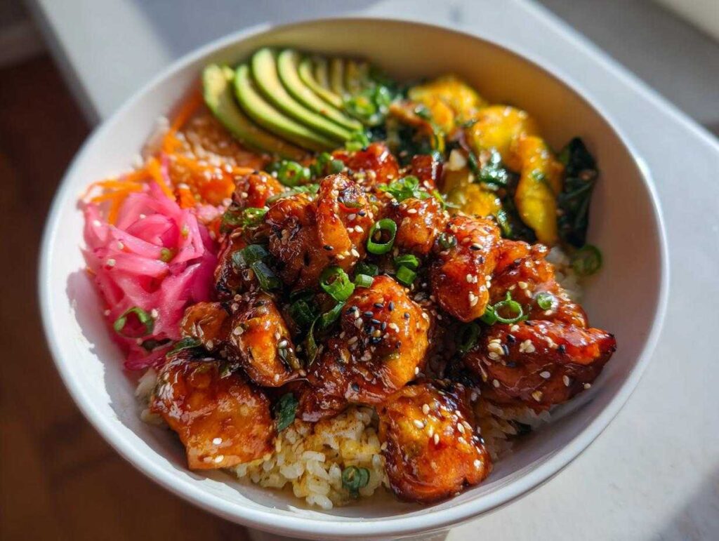 A close-up of a vibrant Hot Honey Chicken Bowl, featuring glazed chicken, rice, sliced avocado, pickled red onions, and greens.