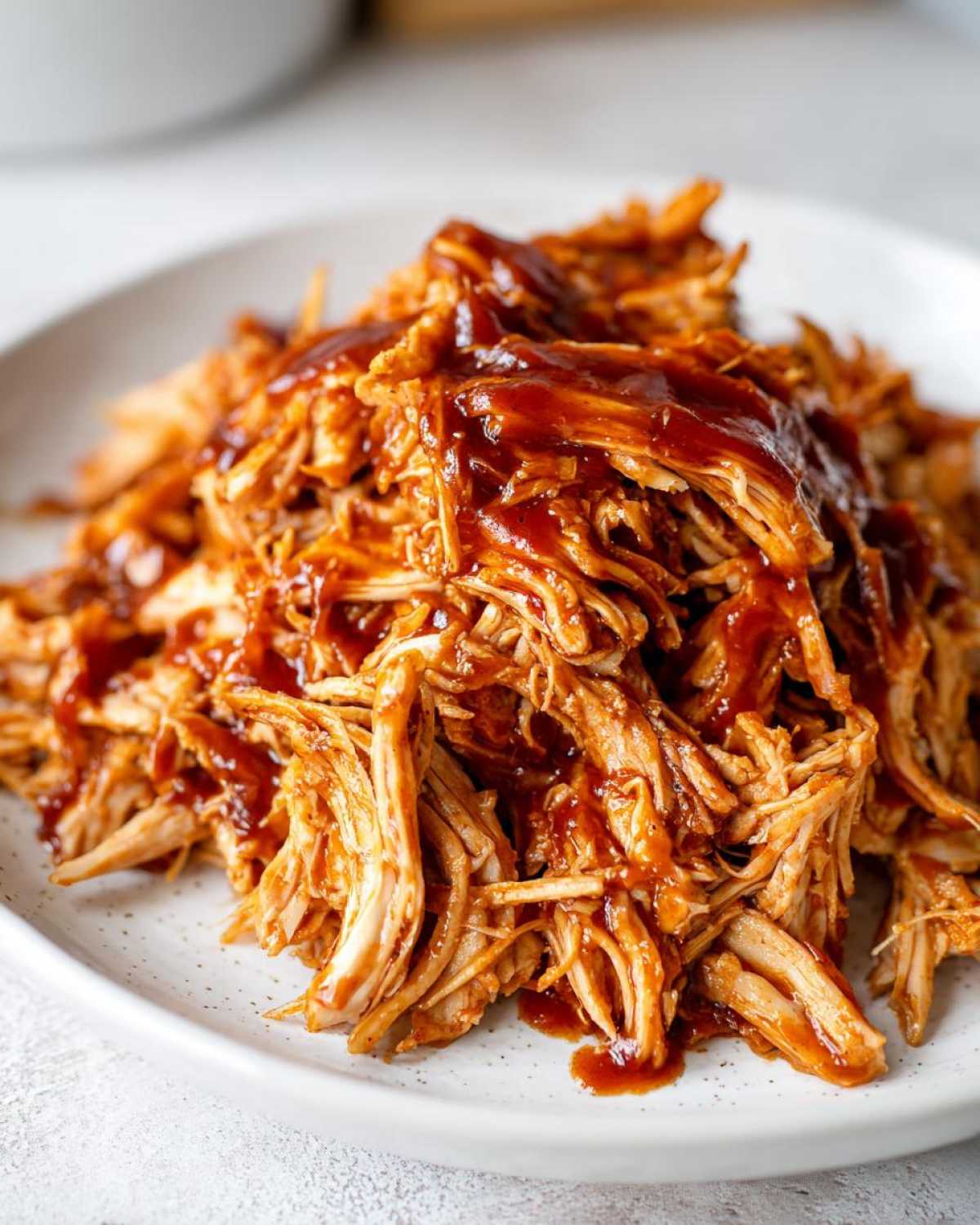 Close-up of a plate piled high with juicy Instant Pot pulled BBQ chicken, drizzled with BBQ sauce.