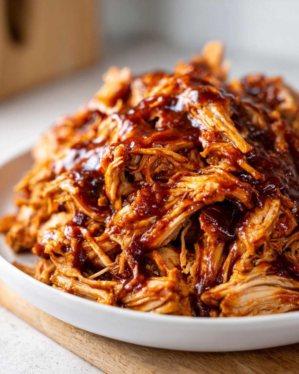 Close-up of a white bowl filled with juicy Instant Pot pulled BBQ chicken, generously coated in rich BBQ sauce.