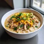 A bowl of creamy Keto cream cheese chicken chili topped with shredded cheese, green onions, and parsley.