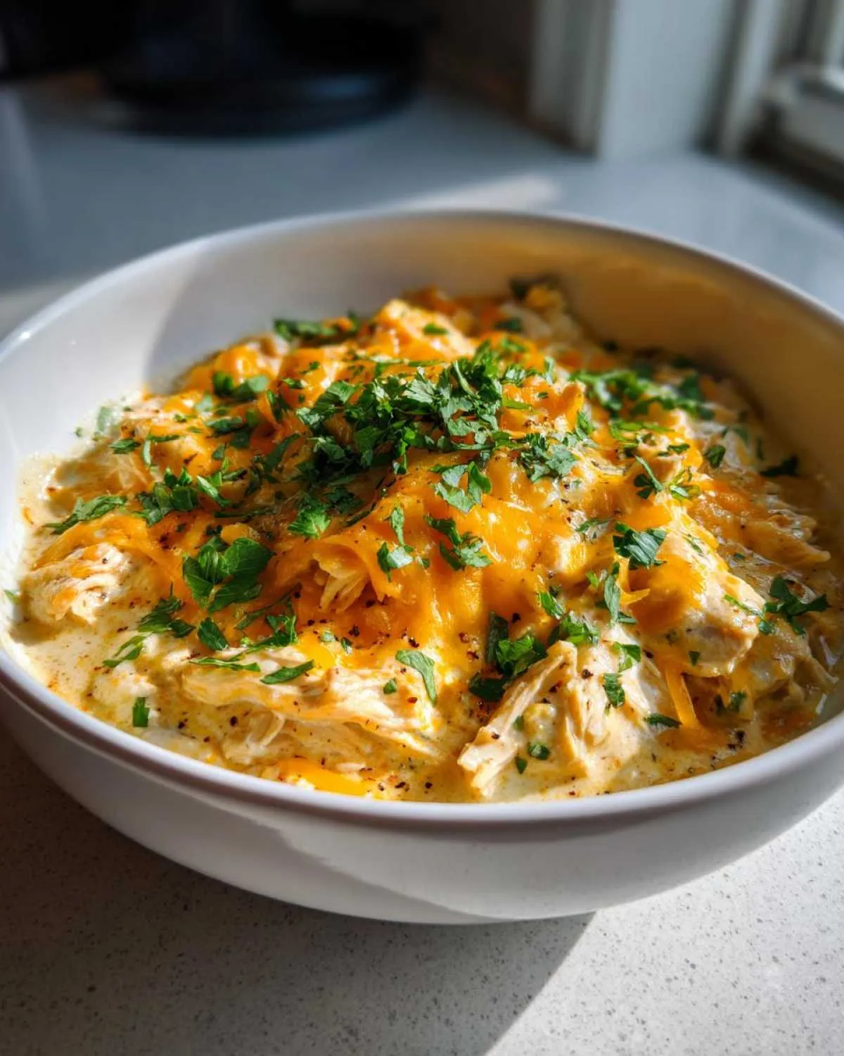 A close-up of a bowl of Keto Cream Cheese Chicken Chili topped with melted cheddar cheese and fresh parsley.