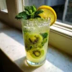 A tall glass filled with a vibrant Kiwi Lemon Mojito, featuring kiwi slices, mint, and a lemon wheel.