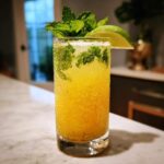 A tall glass filled with a vibrant Mango Mint Mojito Mocktail, garnished with fresh mint leaves and a lime wedge.