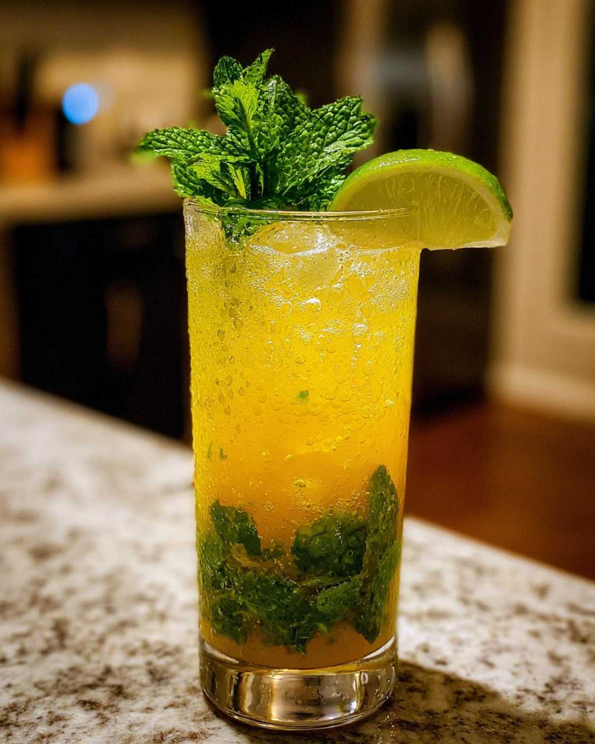 A tall glass filled with a vibrant Mango Mint Mojito Mocktail, complete with fresh mint leaves, lime wedge, and ice.