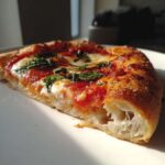 A close-up of a slice of Margherita pizza, showcasing melted mozzarella, rich tomato sauce, and fresh basil leaves.