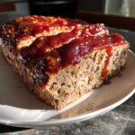 A close-up shot of a slice of meatloaf with glaze, showing the texture of the meat and the glistening glaze.