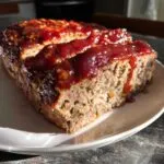 A close-up shot of a slice of meatloaf with glaze, showing the texture of the meat and the glistening glaze.
