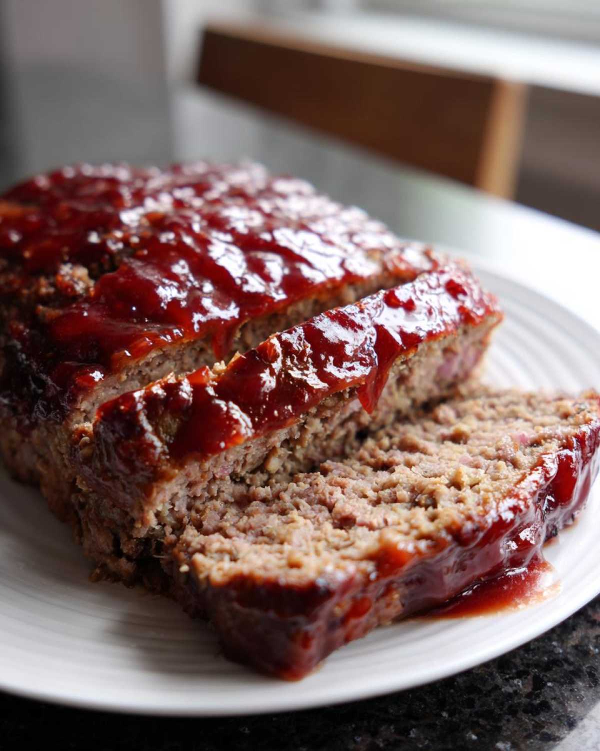 Close-up of a sliced meatloaf with a shiny red glaze, served on a white plate.