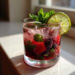 A close-up of a Merry Mint Berry Mocktail with fresh berries, mint leaves, ice, and a lime slice.