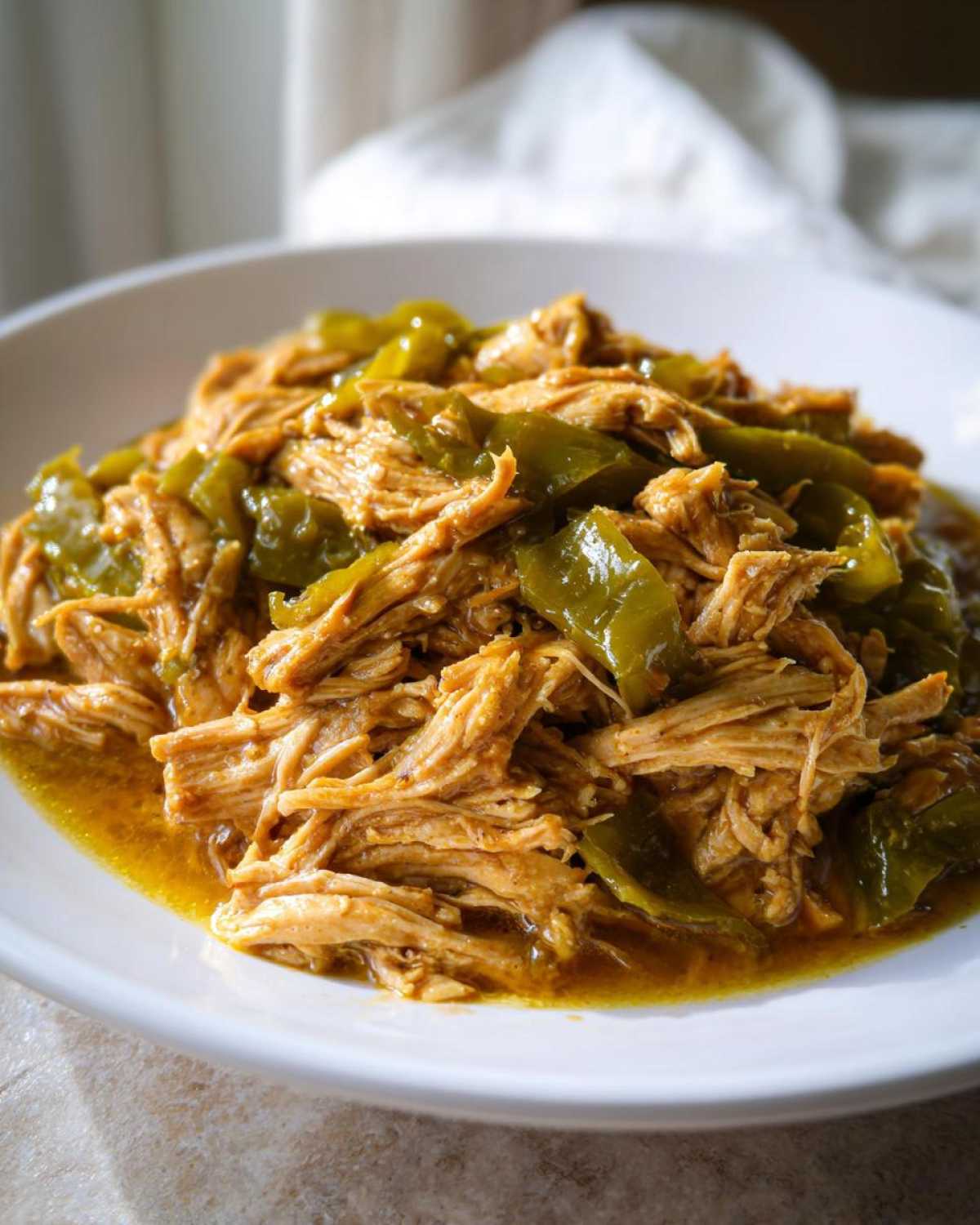 Close-up of shredded Mississippi chicken mixed with vibrant green bell pepper slices in a savory sauce.