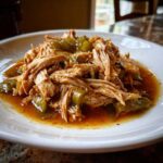 Close-up of shredded Mississippi chicken mixed with chopped green peppers in a savory sauce on a white plate.