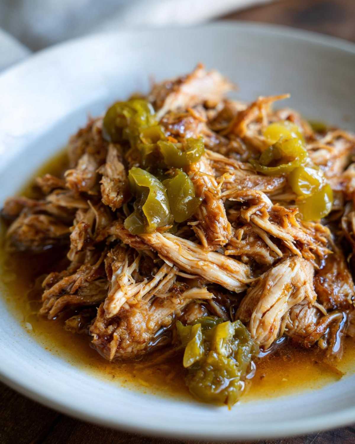 Close-up of shredded Mississippi chicken topped with chopped green peppers in a white bowl.