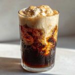 A tall glass of New Orleans iced coffee with a thick layer of whipped cream and a dusting of cinnamon.