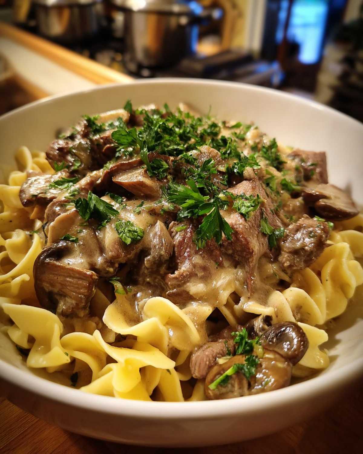 A close-up of a bowl of old fashioned beef stroganoff served over wide egg noodles, topped with fresh parsley.