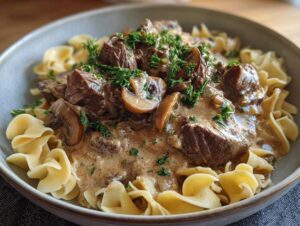 A close-up of a bowl of old fashioned beef stroganoff served over egg noodles and garnished with parsley.