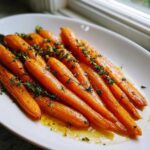 Close-up of tender oven roasted carrots glazed with honey and fresh thyme sprigs on a white platter.
