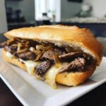 A close-up of a mouthwatering Philly cheesesteak sandwich with thinly sliced steak, melted cheese, and caramelized onions on a hoagie roll.