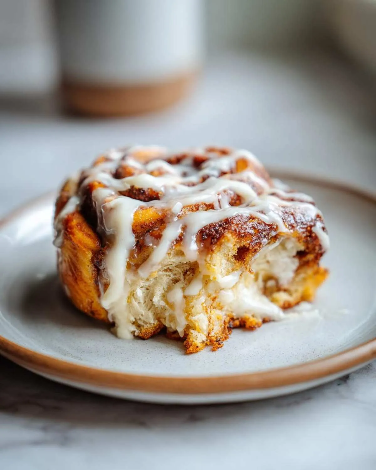 A close-up of a delicious Pistachio Cream Cinnamon Roll, drizzled with white icing and a bite taken out.