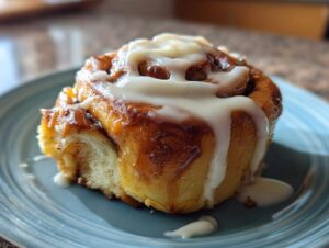 A close-up of a delicious Pistachio Cream Cinnamon Roll drizzled with white icing on a blue plate.