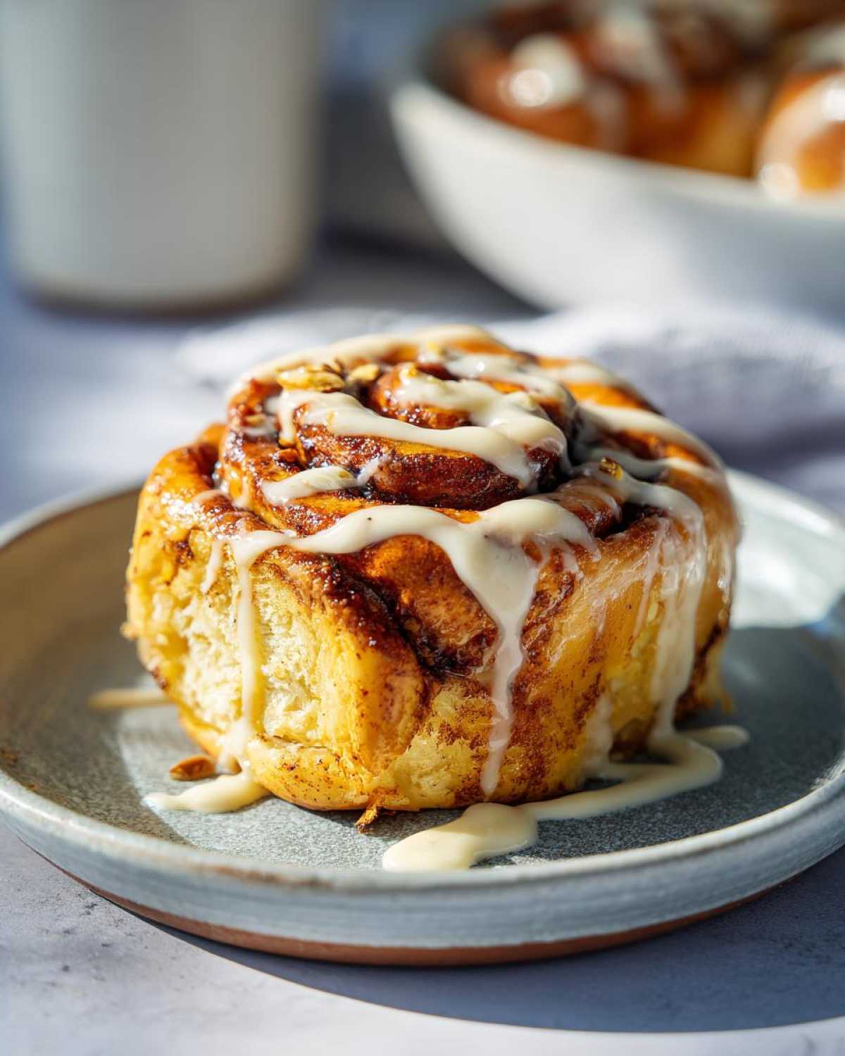 A close-up of a fluffy Pistachio Cream Cinnamon Roll drizzled with white icing on a plate.