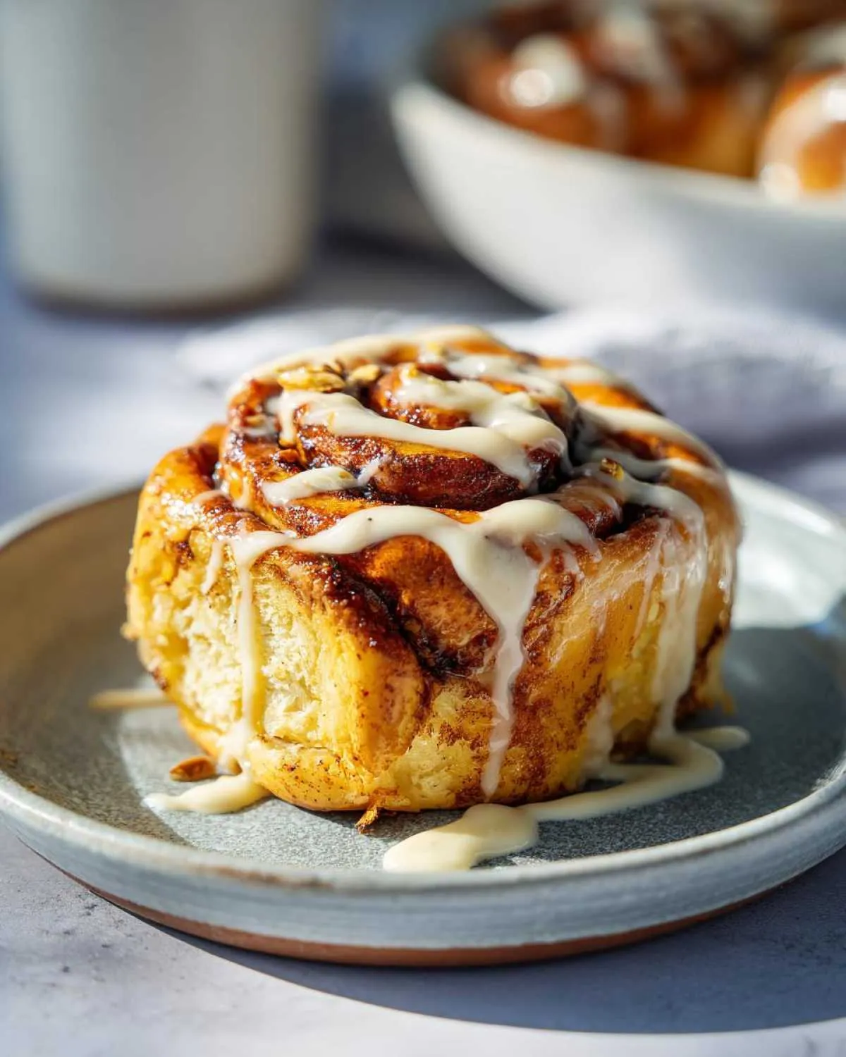 A close-up of a fluffy Pistachio Cream Cinnamon Roll drizzled with white icing on a plate.