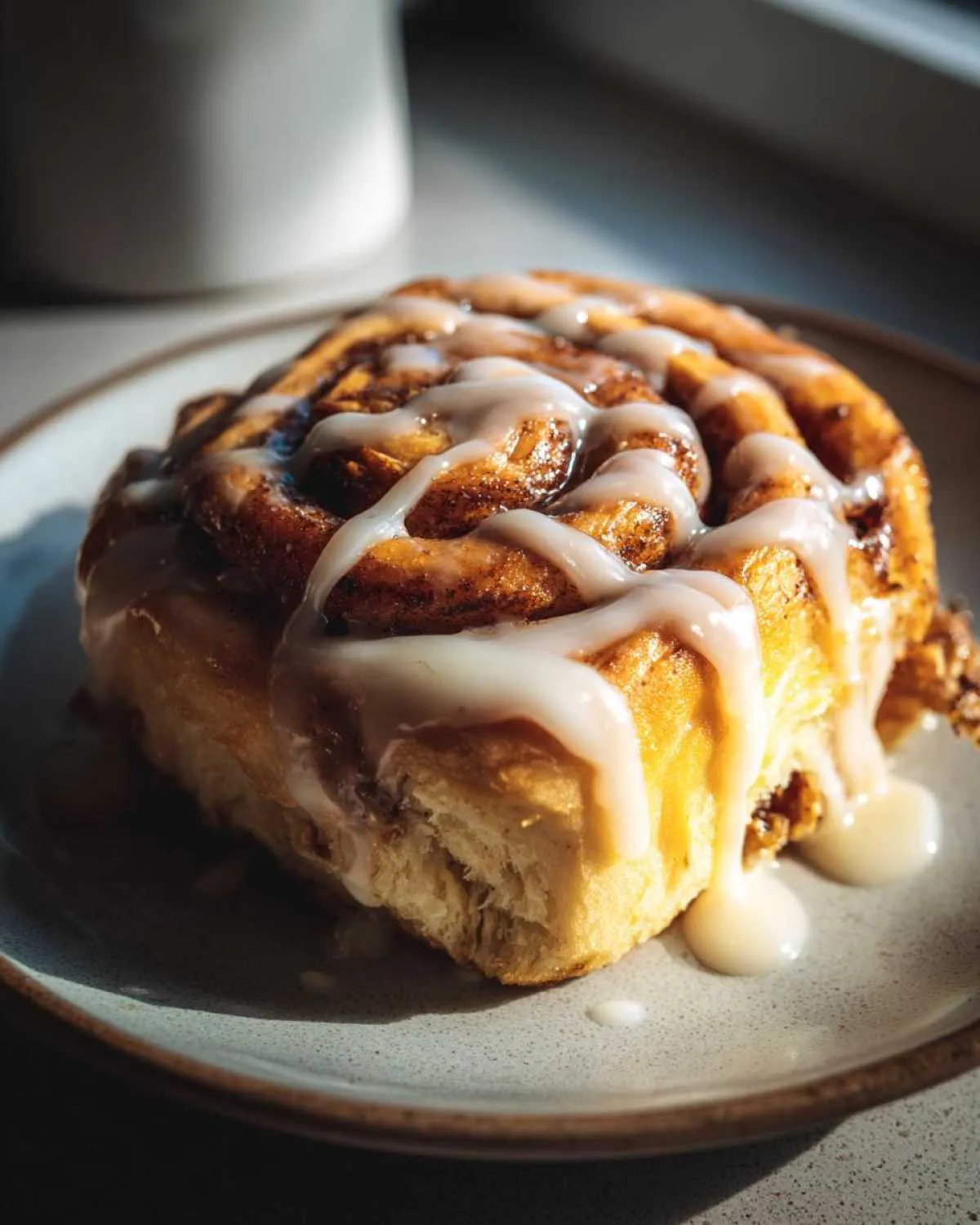 A close-up of a delicious Pistachio Cream Cinnamon Roll drizzled with white icing on a plate.