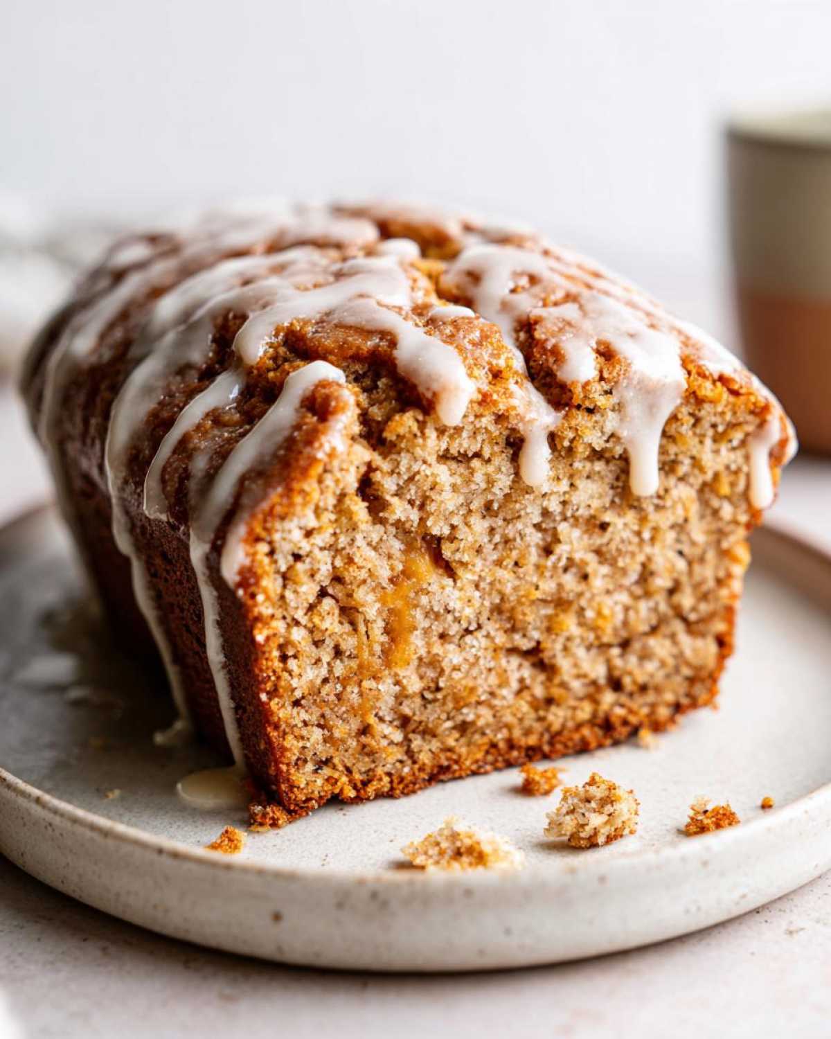 A slice of moist pumpkin banana bread drizzled with white glaze on a plate.