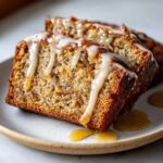 Two slices of moist pumpkin banana bread drizzled with a creamy glaze and syrup on a plate.