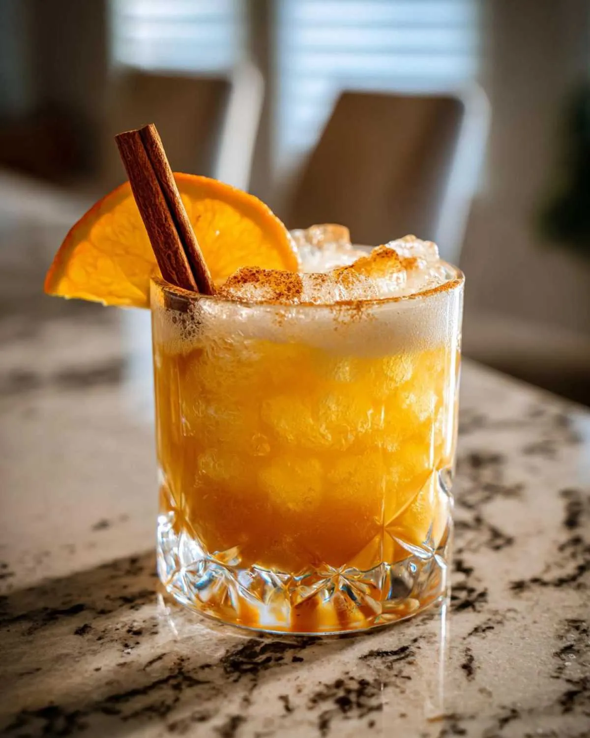 A refreshing Pumpkin Ginger Smash cocktail in a crystal glass, garnished with an orange slice and cinnamon stick, dusted with cinnamon.