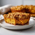 A slice of moist pumpkin oatmeal dump cake with a crumbly topping on a white plate.