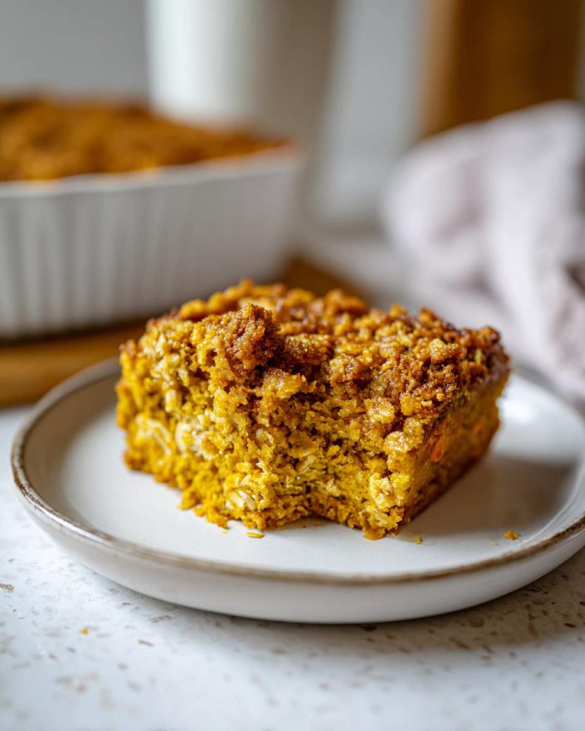 A close-up of a slice of pumpkin oatmeal dump cake on a plate, showing its crumbly topping and moist interior.