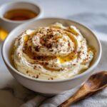 Close-up of creamy Pumpkin Whipped Feta Honey Dip drizzled with honey and sprinkled with spices in a white bowl.