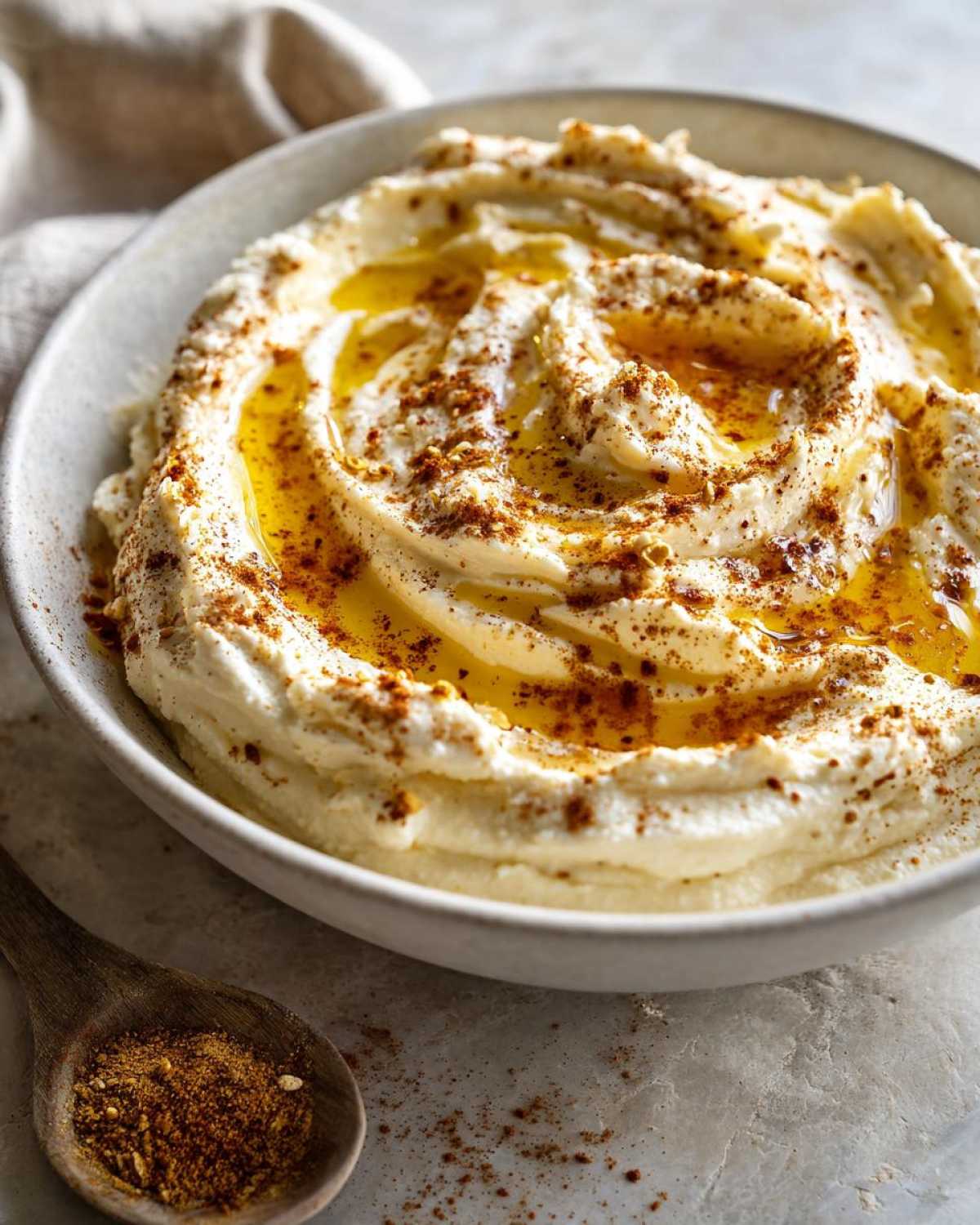 A close-up of creamy Pumpkin Whipped Feta Honey Dip swirled in a bowl, drizzled with olive oil and sprinkled with spices.
