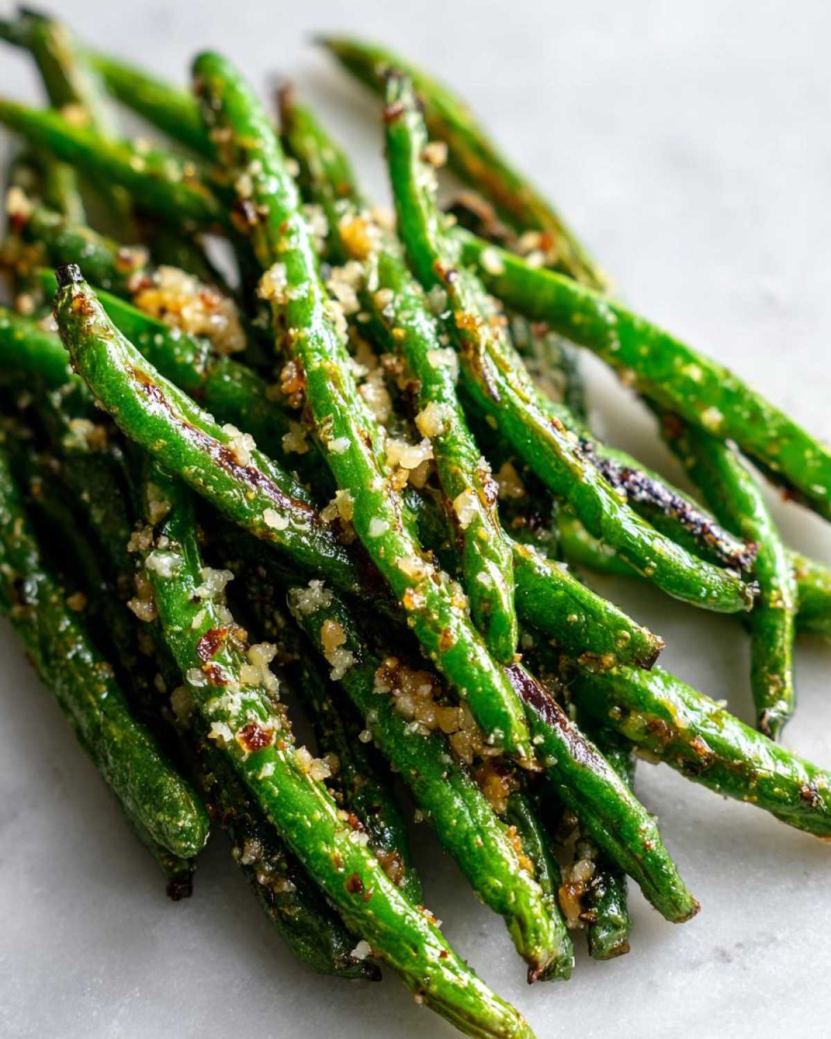 Close-up of crispy roasted parmesan green beans sprinkled with garlic and herbs.