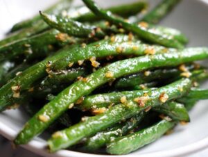 Close-up of glistening roasted parmesan green beans with visible garlic pieces.