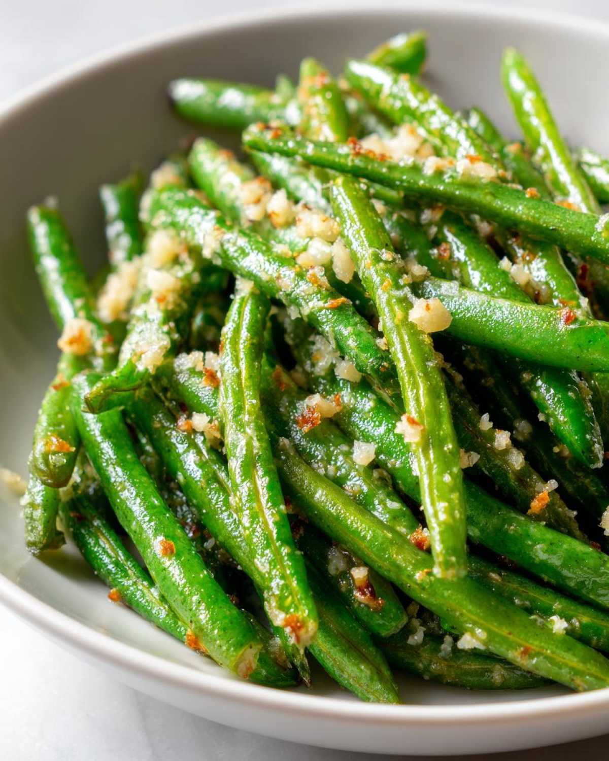 Close-up of a bowl filled with vibrant green beans tossed with parmesan cheese and seasonings, ready to serve.