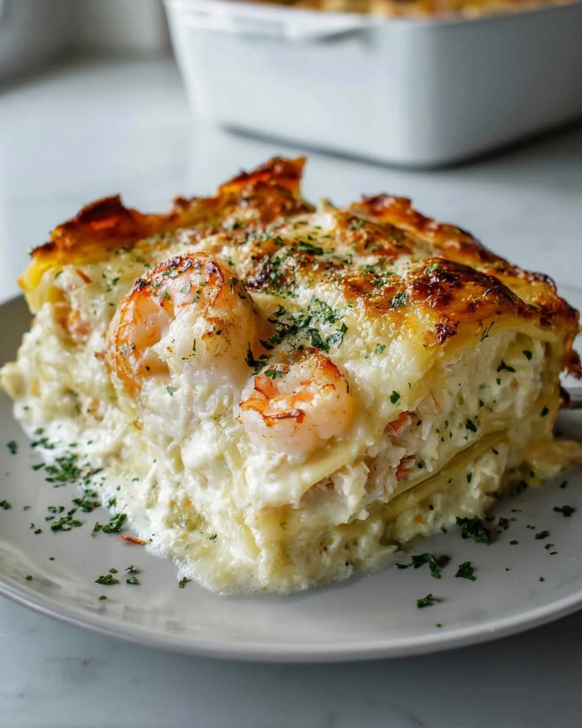 A delicious slice of creamy shrimp crab lasagna, topped with cooked shrimp and parsley, on a gray plate.