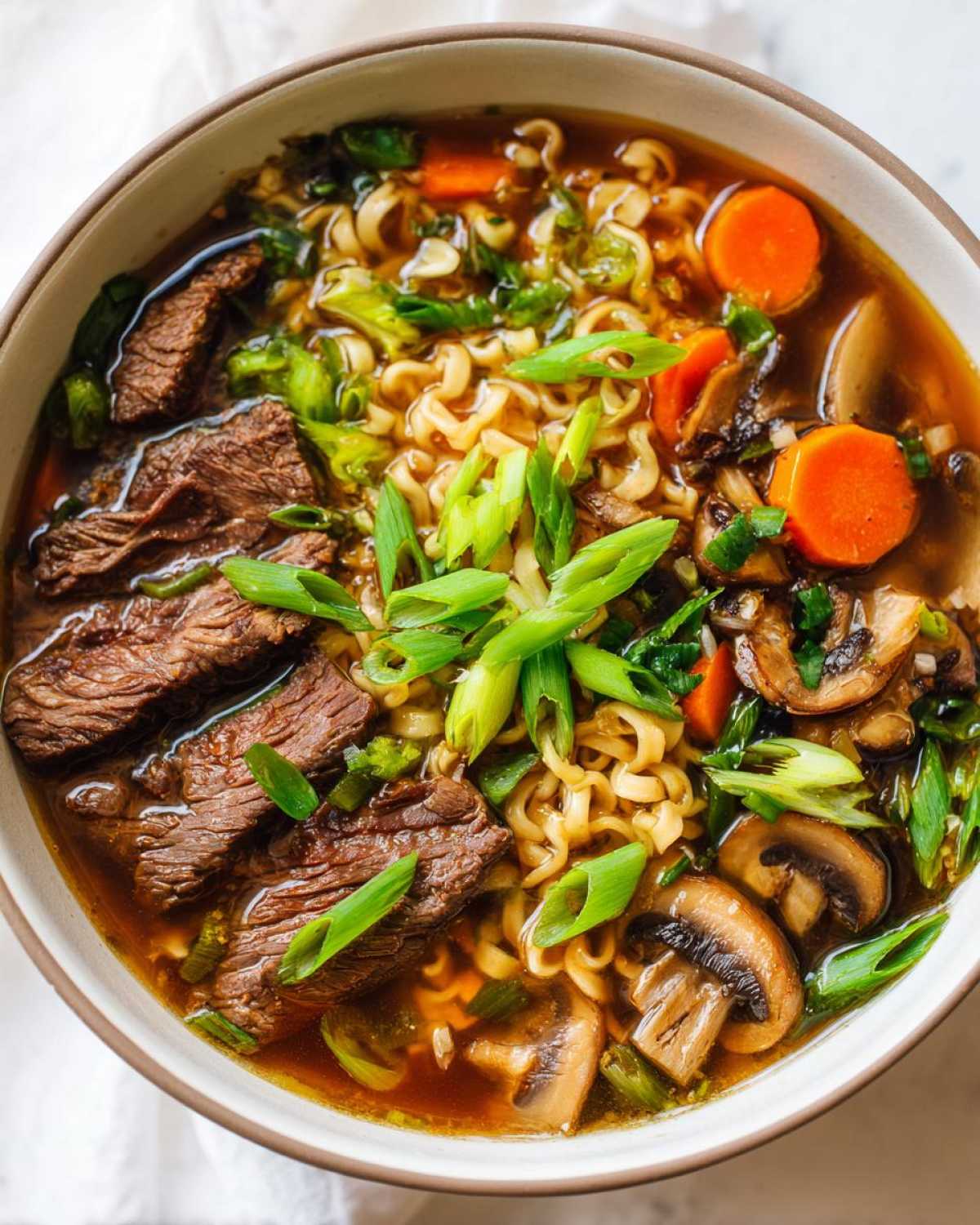 A steaming bowl of slow cooker beef ramen noodles, featuring tender beef slices, ramen noodles, carrots, mushrooms, and green onions.
