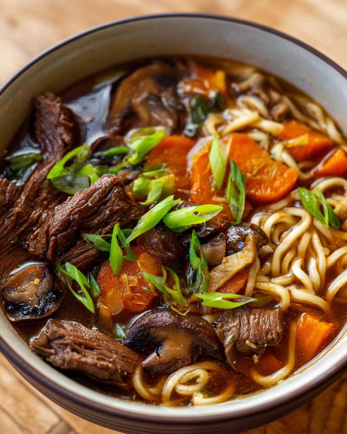 A close-up of a bowl of slow cooker beef ramen noodles with tender beef, mushrooms, carrots, and green onions.