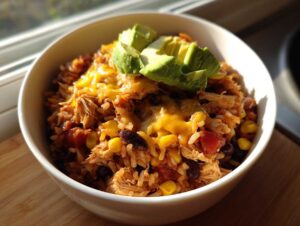 A delicious slow cooker chicken burrito bowl topped with melted cheese and fresh avocado slices.