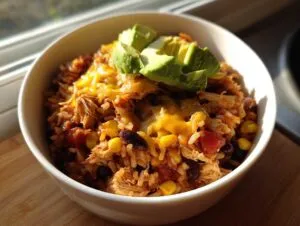 A delicious slow cooker chicken burrito bowl topped with melted cheese and fresh avocado slices.