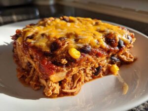 A generous slice of slow cooker chicken enchilada casserole, topped with melted cheese, beans, and corn.