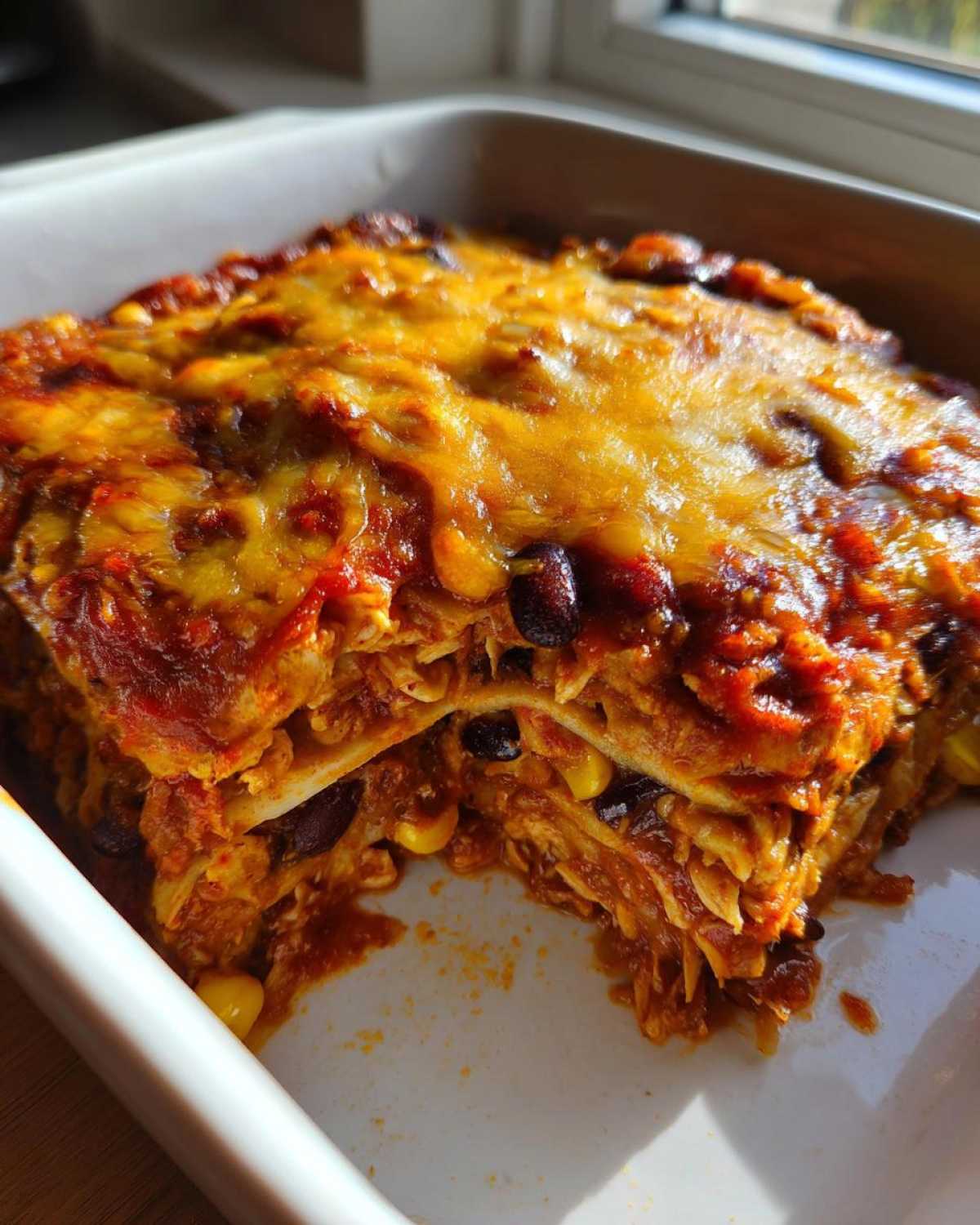 A close-up of a layered Slow Cooker Chicken Enchilada Casserole with melted cheese, beans, and corn.
