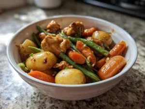 A white bowl filled with slow cooker honey garlic chicken and veggies, including baby potatoes, carrots, and green beans.