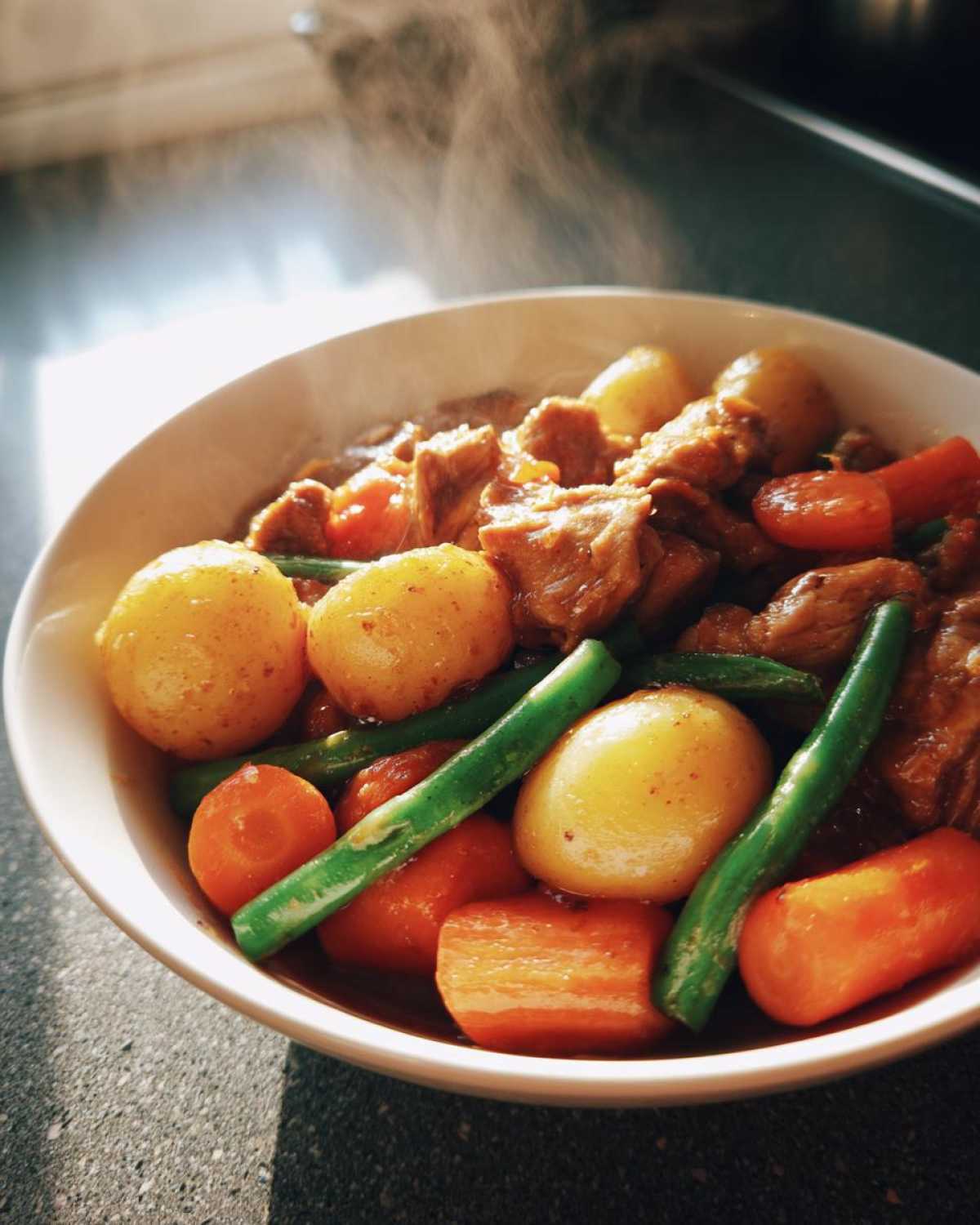 A steaming bowl of Slow Cooker Honey Garlic Chicken and Veggies, featuring tender chicken, potatoes, carrots, and green beans.