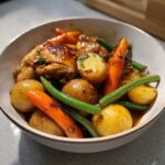 A close-up of a bowl filled with slow cooker honey garlic chicken and veggies, including potatoes, carrots, and green beans.