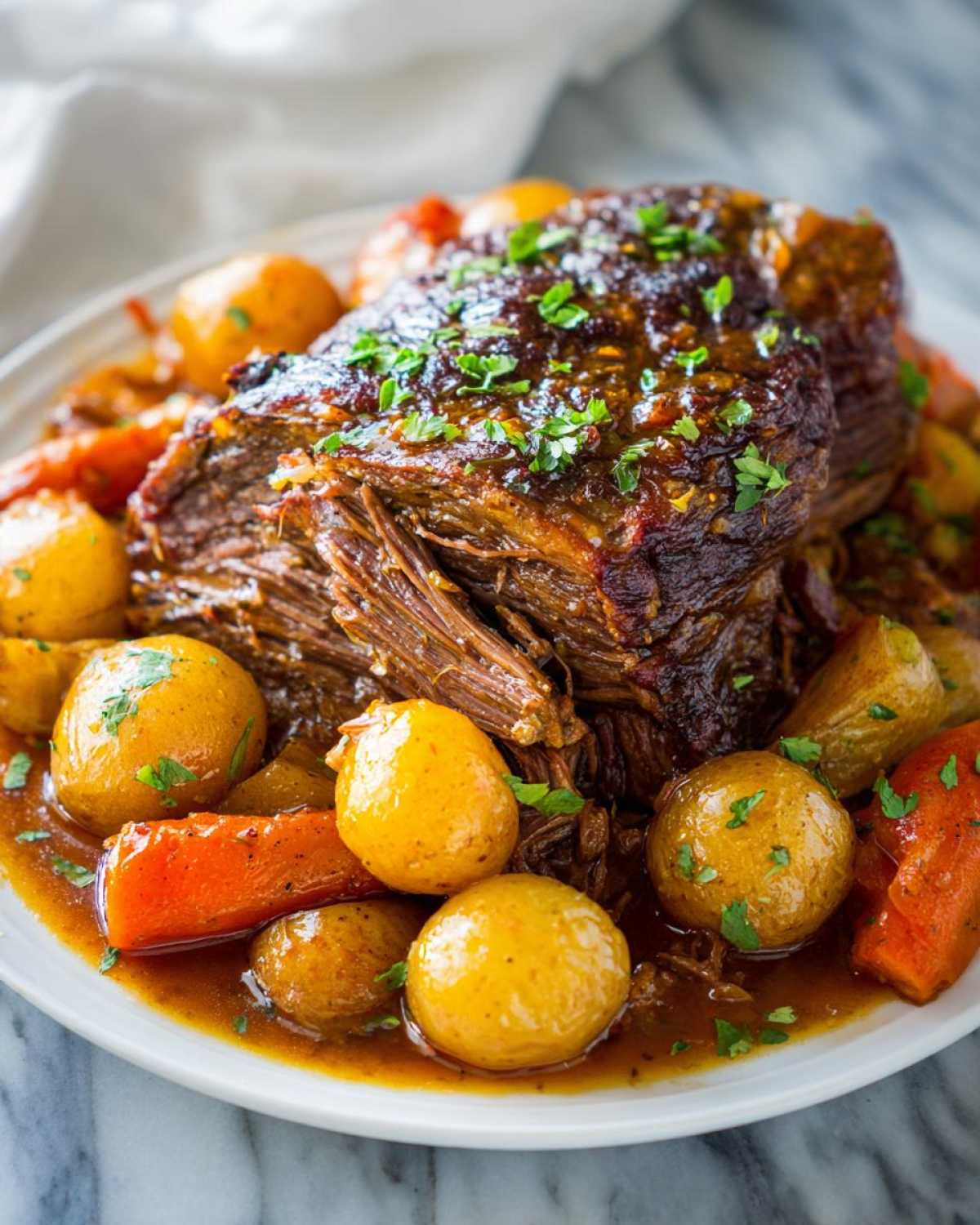 A close-up of a tender slow cooker pot roast surrounded by baby potatoes and carrots, garnished with parsley.